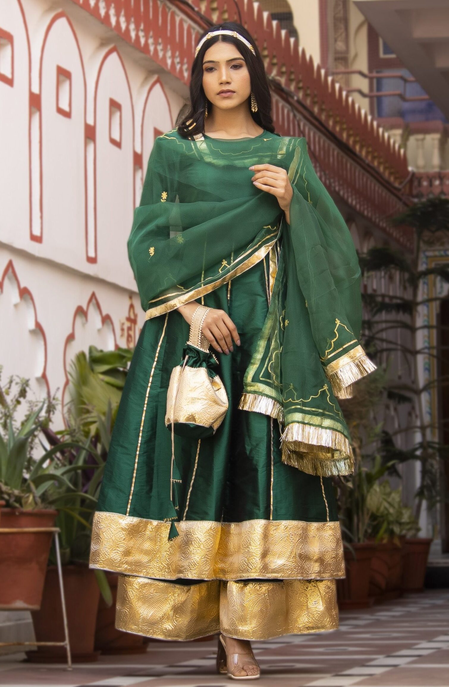 Green taffeta silk sharara set with long kurta featuring gota detailing and three-quarter sleeves, matching sharara with gota border, green organza dupatta with aari embroidery and gota accents, and coordinating potli in Golden Muslin by Priyanka Rathore