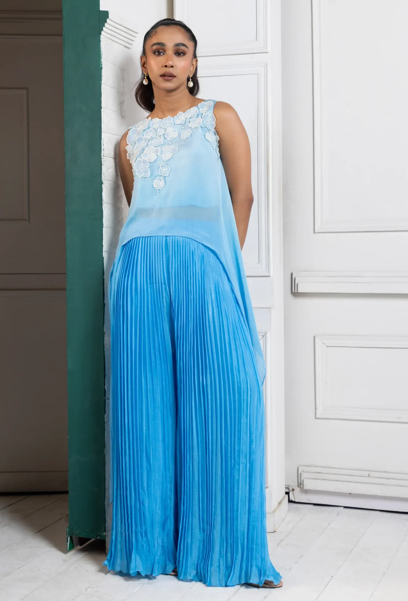 Model wearing sky blue golden muslin asymmetric chiffon cape with pleated cascade pants