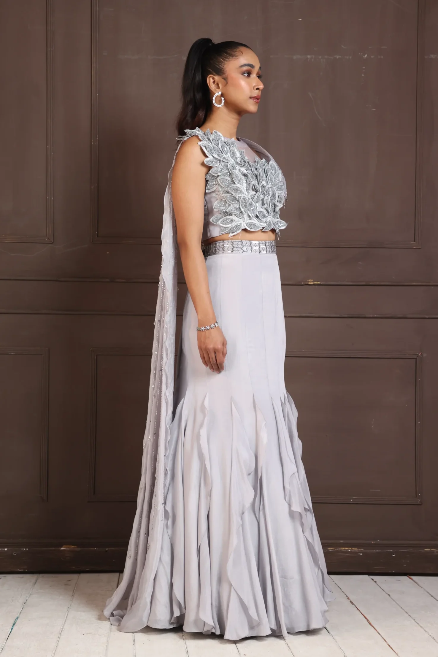 Model wearing silver petal golden muslin embellished lehenga set with 3D floral crop top and ruffled flared skirt
