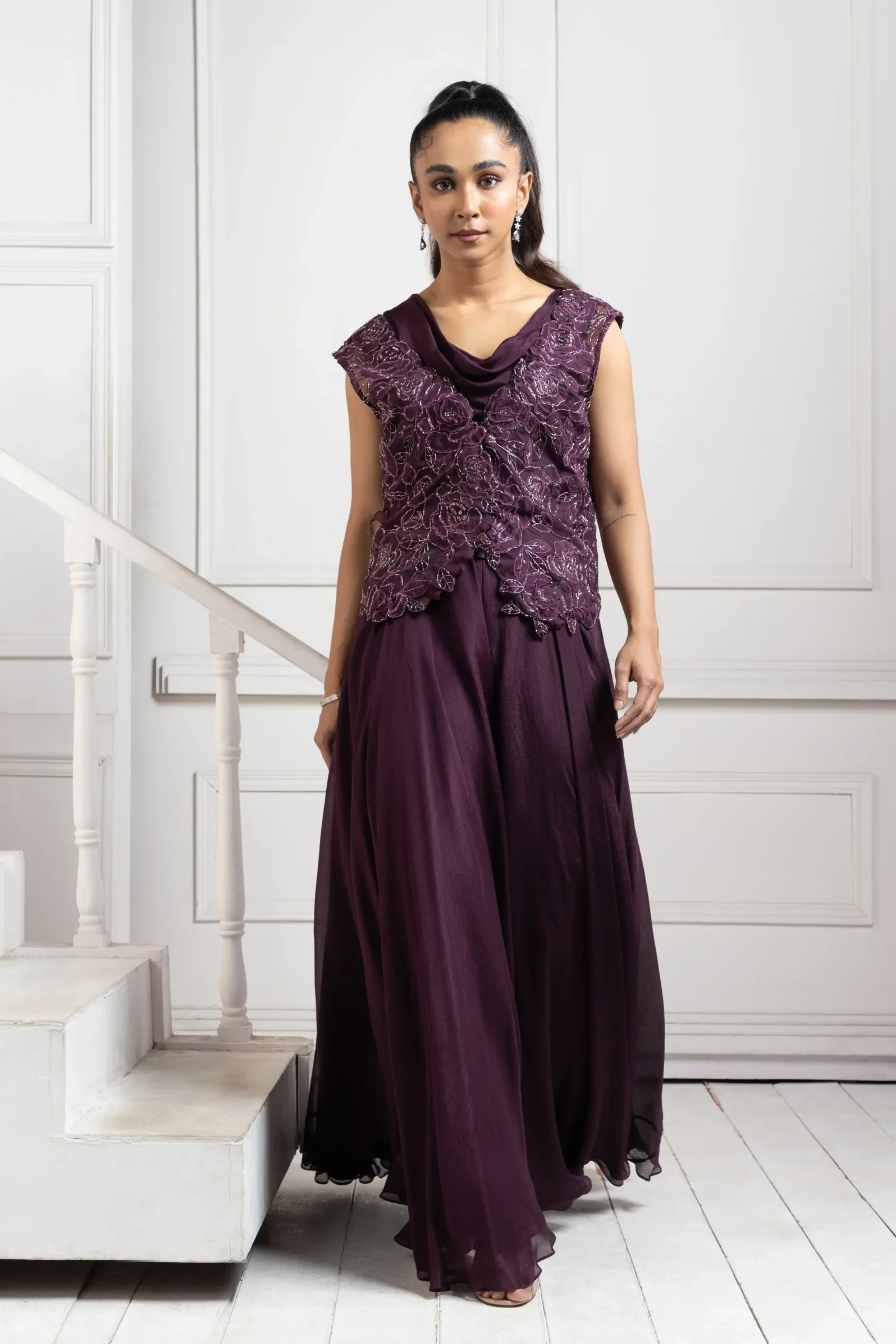 Model wearing deep plum golden muslin embroidered ensemble with wide leg trousers and floral appliqué bodice
